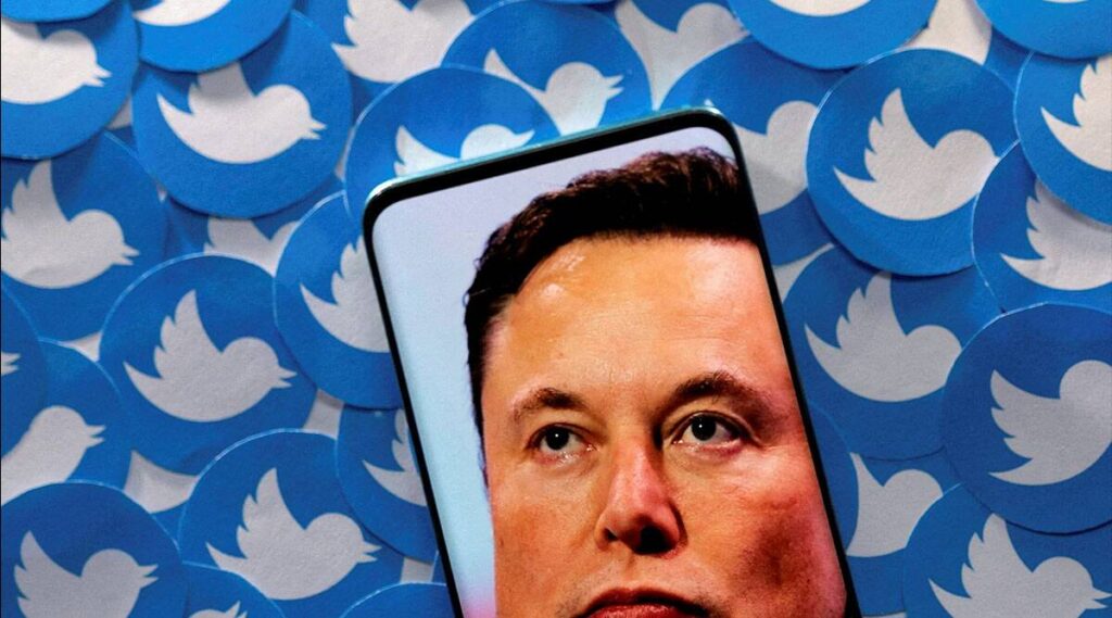 An image of Elon Musk is seen on a smartphone placed on printed Twitter logos