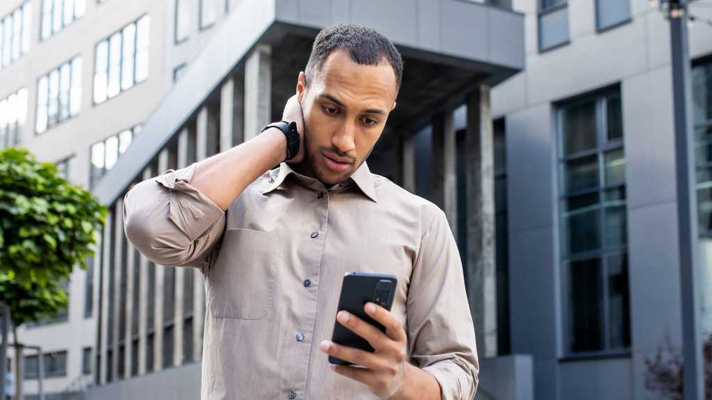Qualcomm Chip Vulnerability Leaves Android Phones at Risk Dunkelhäutiger Mann blickt ratlos auf sein Handy